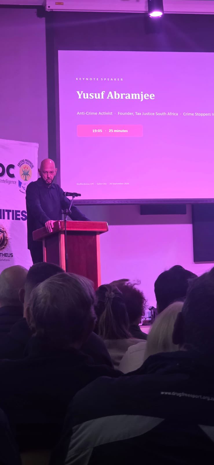Yusuf Abramjee at the podium beside the keynote-speaker slide